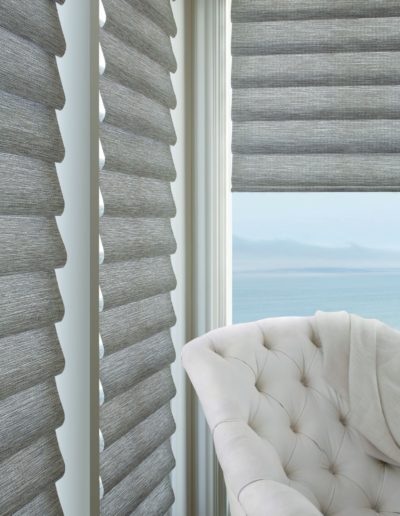 Light gray roman pull shades with white chair overlooking sea